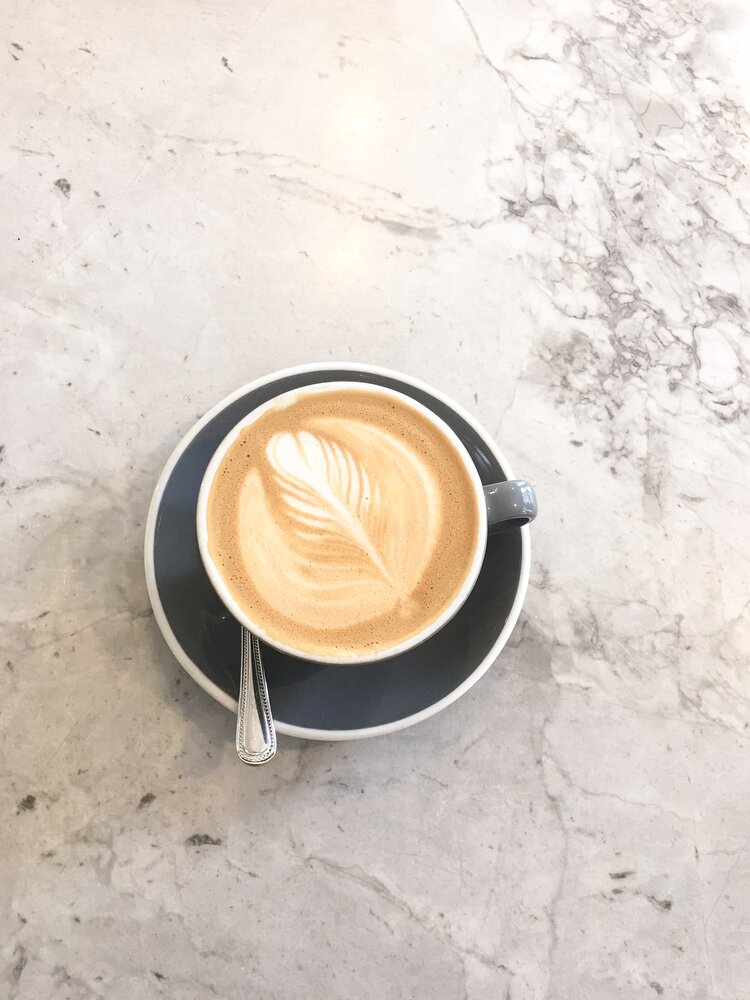 Almond milk latte in blue cup and spoon on marble table