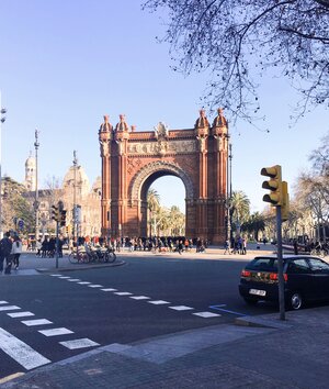 Arc de Triomf from across the street on a sunny day with a small black car parked on the street curb
