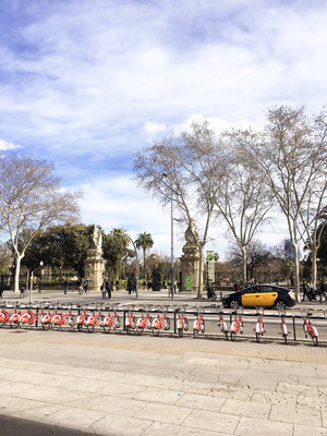 Ciutadella entrance in Barcelona Spain with a black and yellow cab passing in front and city bikes lined up