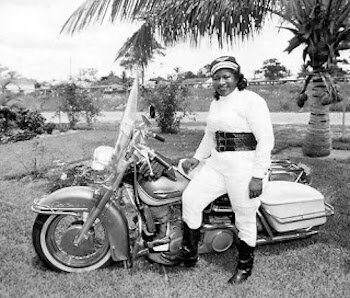 Black History woman Bessie Stringfield smiling and half sitting on a white motorcycle