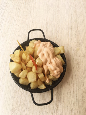 Black bowl of hot patatas bravas with one yellow toothpick and one red toothpick