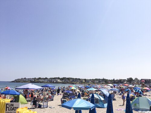 Busy beach with lots of blue umbrella shades open on the sand in York Maine