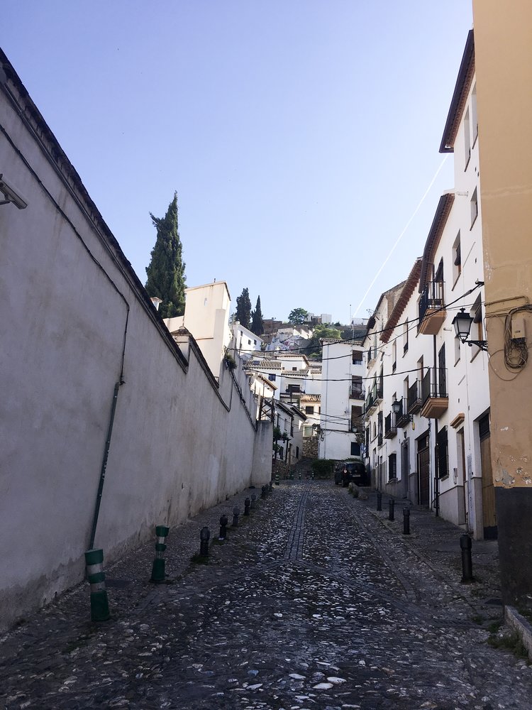 Cobblestone street up a small alley in Granada along white buildings