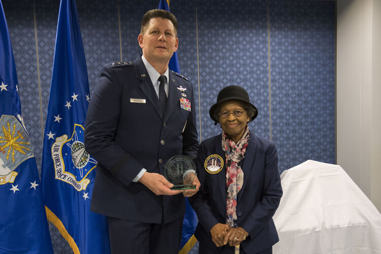 Dr. Gladys West in a blue suit and floral-printed scarf standing with Lt. General DT Thompson in uniform getting inducted into the Air Force Pioneers Hall of Fame.