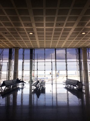 Half empty airport with one person seated and a Ryanair plane outside the window