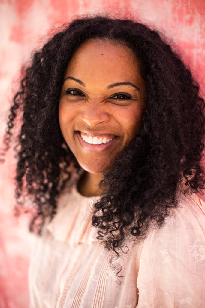 Kim smiling in a light pink shirt in front of a pink wall