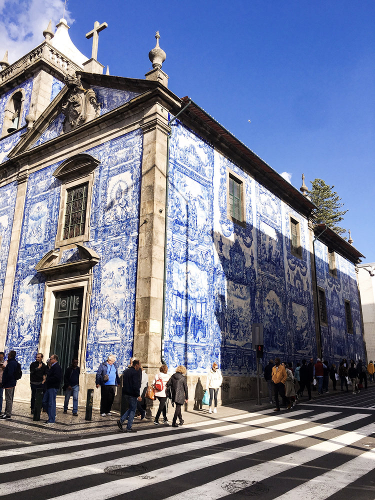 People walking in front of the east side of the bright blue Chapel of Santa Catarina in solo female travel Europe destination Porto Portugal on a sunny afternoon