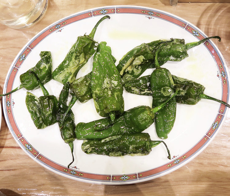 White plate of bright popular tapas green padron peppers with cracked sea salt and olive oil drizzle