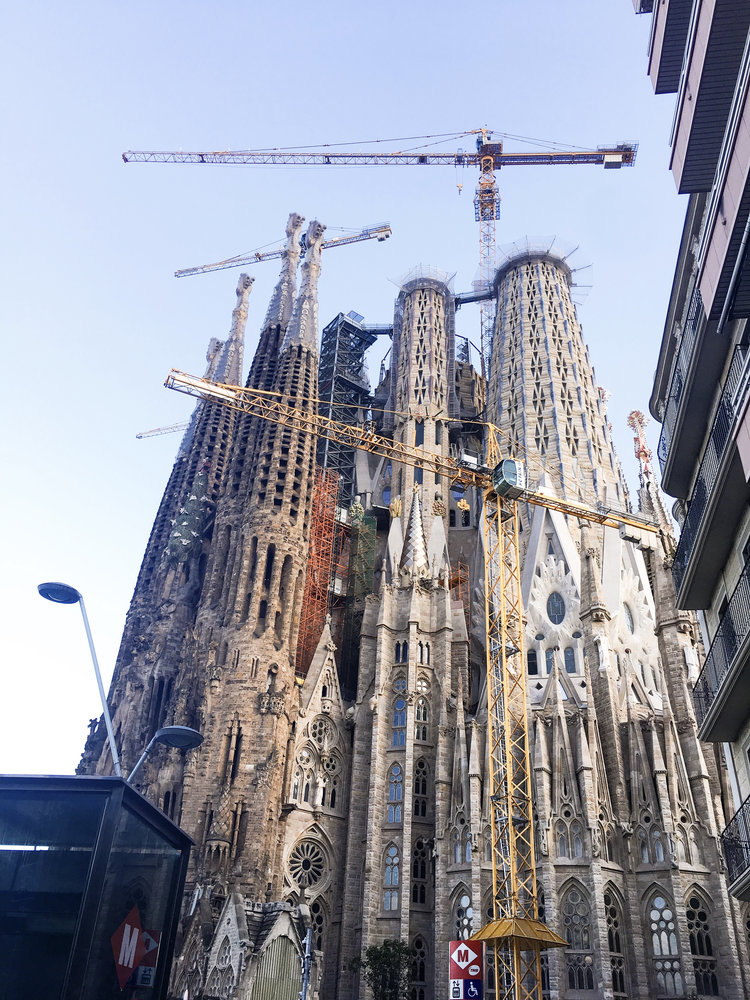 Sagrada Familia with yellow crane in front of it and the metro beside it on a sunny day