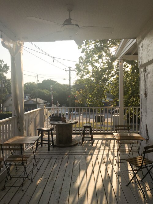 The outside upper deck of Gilly Brew Bar with empty wooden tables looking out at the railroad