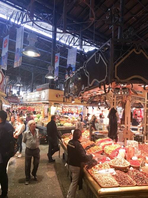 Tourists walking among stalls with spices and fruit inside Boqueria Market
