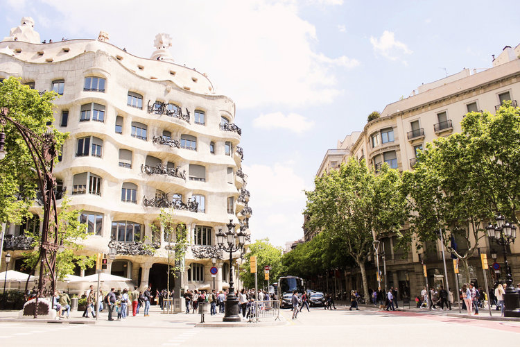 Tourists walking along Passeig de Gracia and Carrer de Provenca by Antoni Gaudi’s La Pedrera building in Barcelona