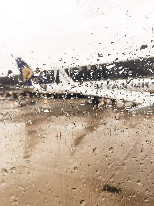 Blurry view of Ryanair plane sitting on the tarmac at the airport through a plane window with rain drops on it
