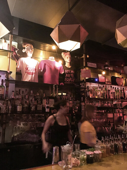 Butter and Scotch at night with with bartenders working and bottles of liquor and t-shirts on display