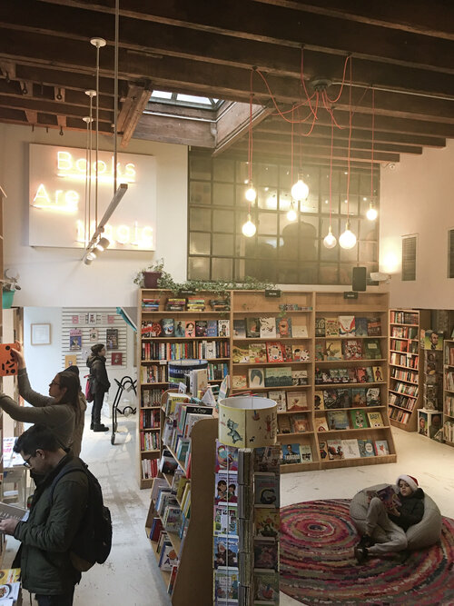 Inside of Books are Magic with tall brown bookshelves filled with books and customers sitting on bean bags and examining the books on the shelves