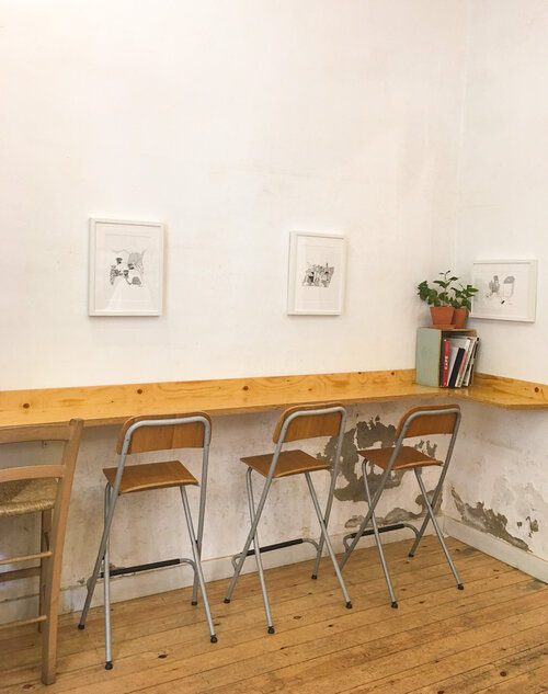 Inside Slow Mov coffee shop with wooden bar and three wooden chairs and three white framed paintings