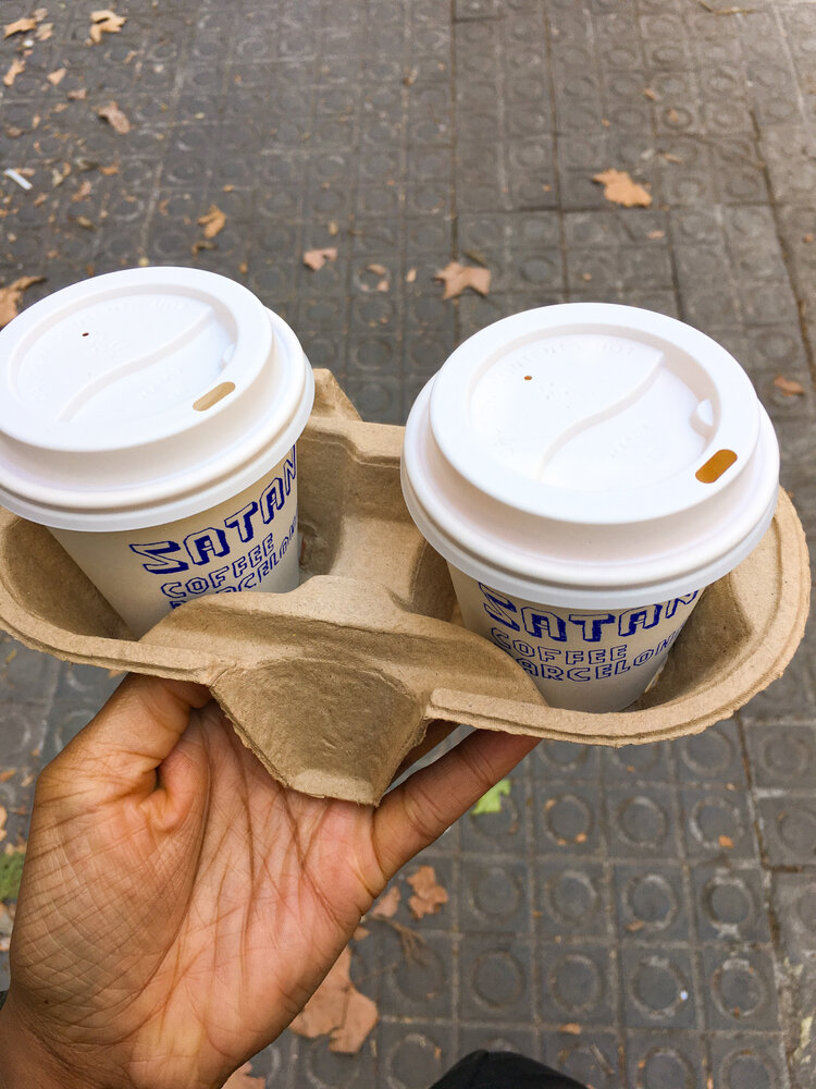 Kim holding two to go coffee cups from Satan’s Coffee Corner on the sidewalk in Barcelona Spain