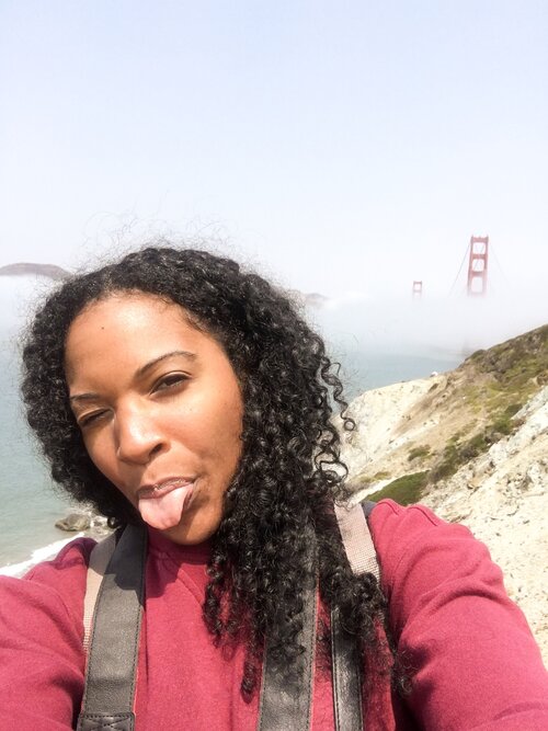 Kim in front of the golden gate bride in San Francisco California traveling alone on a sunny day wearing a red sweater and sticking her tongue out