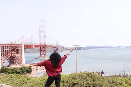Kim making the peace sign in the air on her first time traveling alone wearing a red sweater in front of the golden gate bride