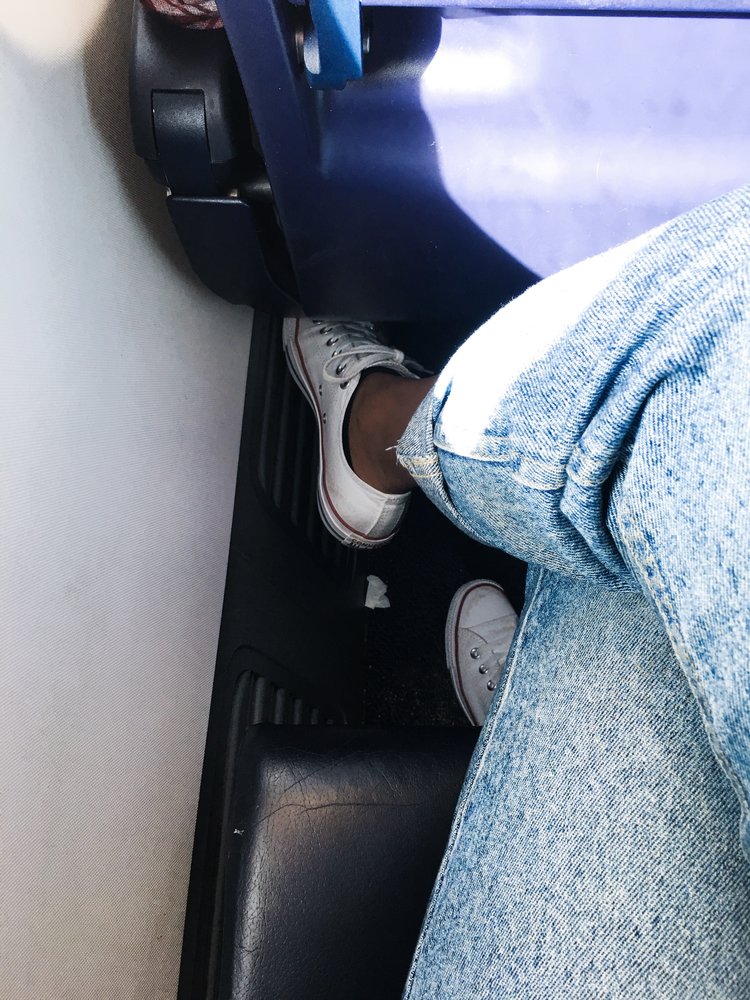 Kim flying with Ryanair sitting with legs crossed wearing blue jeans and white converse sneakers on a tight Ryanair flight
