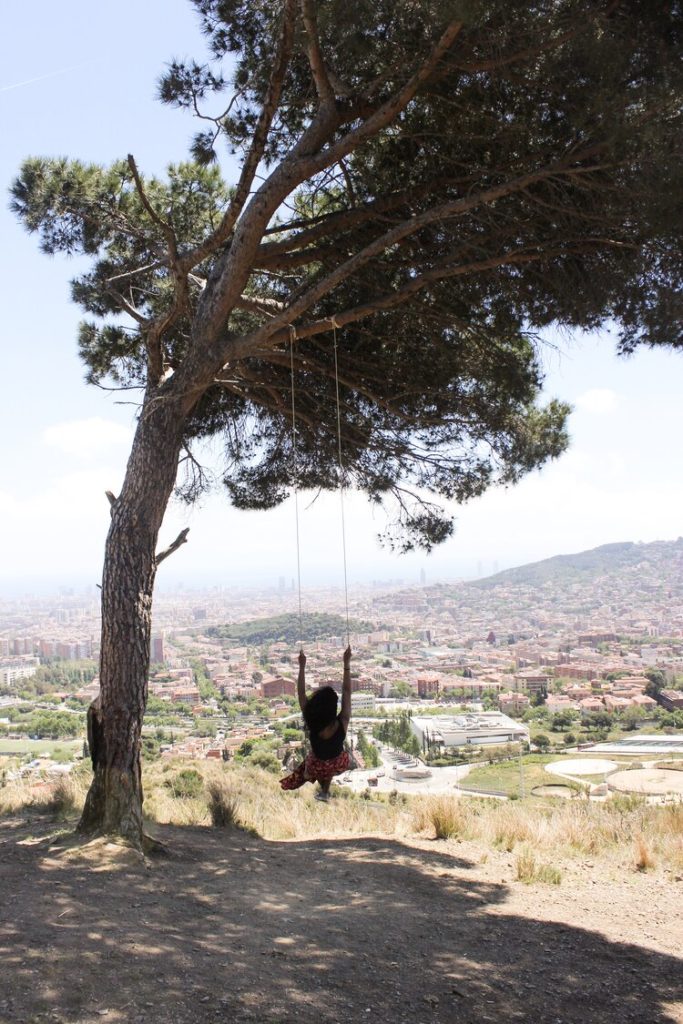 Kim swinging from a tree solo traveling and looking out at the view of Barcelona on a sunny afternoon