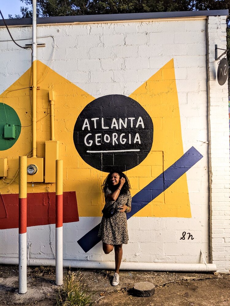 Kim wearing a floral dress and a black fanny pack in front of a brightly colored atlanta georgia mural in the evening