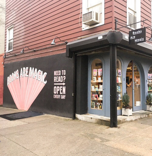 Outside of Books are Magic in New York City with pink and white mural on the left side wall