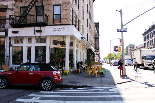 Outside The Butcher’s Daughter with small red car parked in front of it on a sunny afternoon