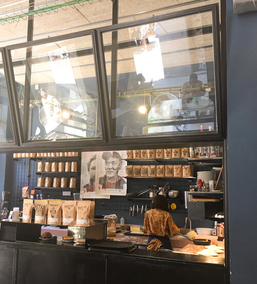 Large open counter at Satan’s Coffee corner with lots of coffee for sale on the shelves and woman working behind the counter