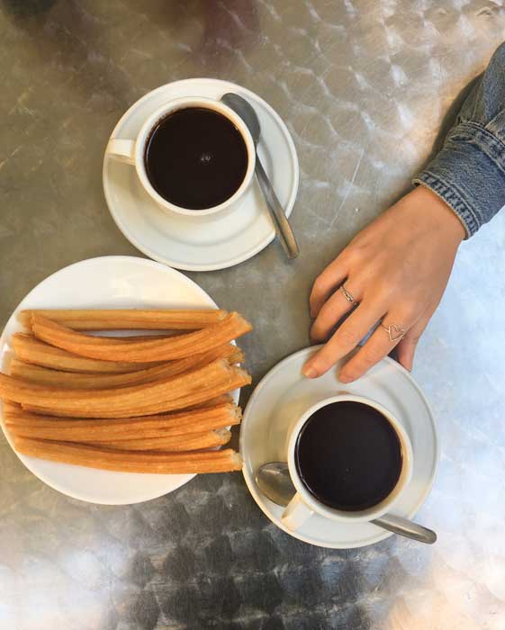 Madrid vs. Barcelona travel plate of churros and two mugs of chocolate on a metal table
