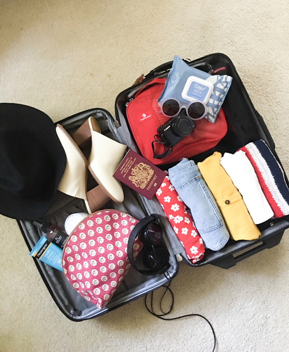 Bird's eye view of packed open suitcase with clothes, passport, and travel accessories. How to pack a carry on blog post.