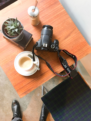 Bird's eye view of a DSLR camera and a latte on a table top. How to pack a carry on blog post.